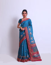 The blue semi-Tussar saree with a pink border featuring Pichwai design adds a touch of cultural richness and elegance to the ensemble - BLN00855
